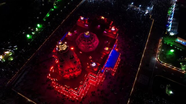 Aerial drone view of the beautifully illuminated Prem Mandir in Vrindavan, India, during Janmashtami celebrations at night. The magnificent temple glows with colorful lights that continuously change.