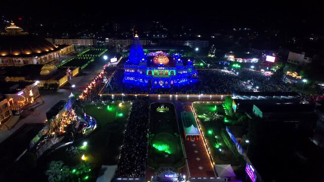 Aerial drone view of the beautifully illuminated Prem Mandir in Vrindavan, India, during Janmashtami celebrations at night. The magnificent temple glows with colorful lights that continuously change.