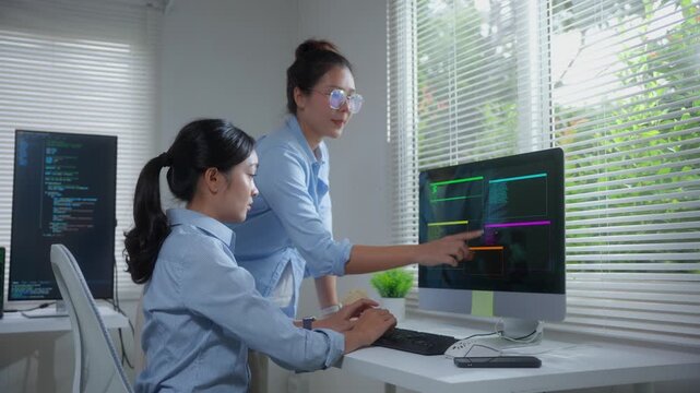 Two female asian programmers coding and collaborating on a new software development project in a modern office