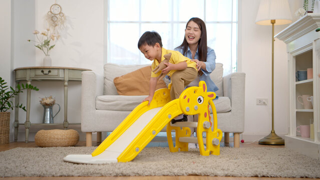 Happy little boy sliding down with laughter while his mother watches nearby