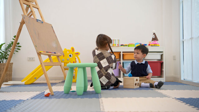 Little girl drawing while a boy walks around, reflecting independent activities