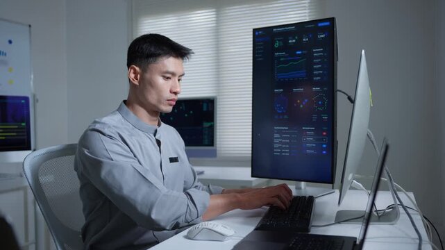 Asian data scientist working on a computer analyzing statistics and graphs in a modern high tech office with multiple screens