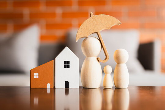 Real estate home property insurance and family protection concept, wooden figure parents with child holding umbrella shielding house model against risk, representing mortgage loan safety.