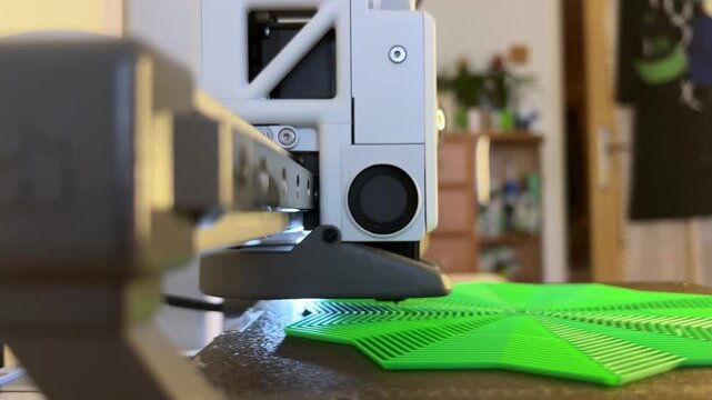 A 3D printer is printing a toy model of a green anti-stress star.
