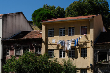 Laundry drying on a clothesline across a yellow house facade with tiled roofs in Guarda, Portugal. Traditional residential architecture and everyday domestic life for travel and housing themes. © Renata
