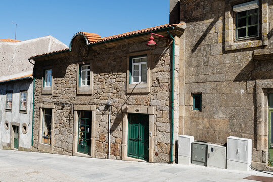 Old granite stone house with green doors, white windows and terracotta tile roof on a sunny street in Guarda, Portugal. Historic architecture for travel and heritage tourism.