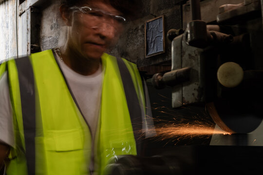 Middle aged Asian small business owner inside his old family machine shop, dad heavily motion-blurred bending toward the machine as a wide spray of sparks, craftsmanship and dedication