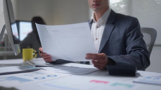 Businessman working overtime analyzing financial documents and data charts at his desk in a modern corporate office at night