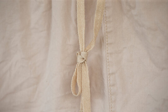 Close up of beige cotton drawstring knot on wrinkled fabric texture.A high-quality close-up macro shot focusing on a soft beige or cream-colored woven drawstring tied into a knot on a matching cotton 