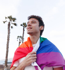 A young man proudly walks along the seashore carrying the LGBTQ flag © G.S.Rob