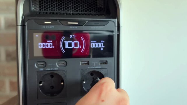 Close up of a woman's hand pressing the power button and plugging a cable into a fully charged portable power station, a modern device for off grid and backup electricity