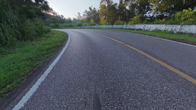 POV road cycling along a winding mountain road surrounded by lush green forest, with a curved roadway, white roadside barrier and peaceful natural scenery.