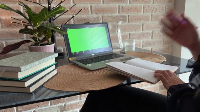 Professional female therapist or coach sitting at a desk, providing mental health support during a remote video consultation, gesturing and writing in a notebook