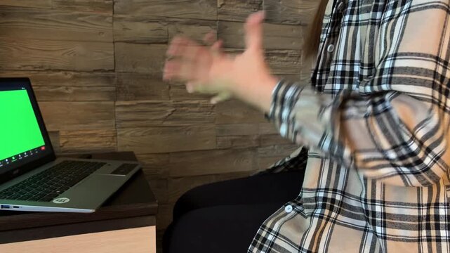 Woman gesticulating during an online therapy session with a laptop showing a green screen, expressing her emotions and feelings to a psychologist in a video call at home