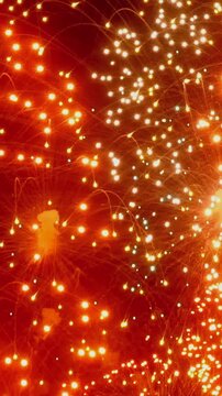 Vertical video shows fireworks display in night sky background. The frame also shows abstract light pattern and visual texture against black background within night sky background.