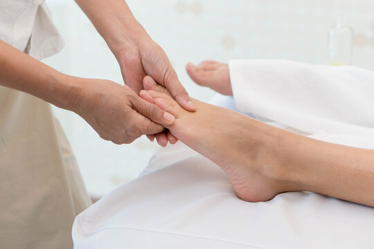 Close up of therapist hands massaging client foot in spa salon, professional foot reflexology treatment for young Asian woman, wellness relaxation and healthcare concept