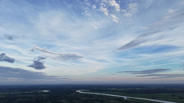 Aerial view of winding river through lush green countryside at sunset with dramatic cloudscape drone