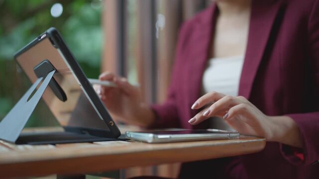Businesswoman multitasking with tablet and smartphone at an outdoor cafe while working remotely on a wooden desk
