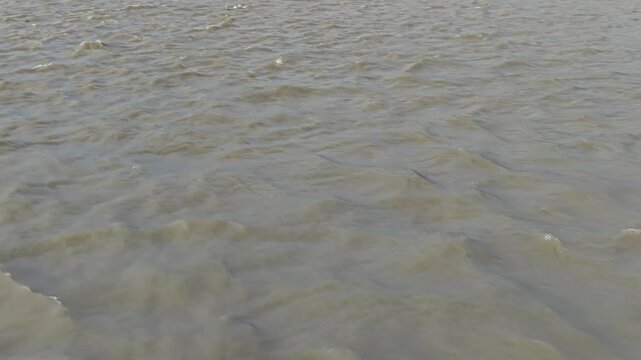 Rippling murky river water surface background, flowing brown water texture, natural river current motion