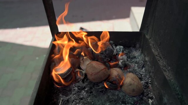 Close up slow motion shot of coconut shells burning amidst bright flames in a metal brazier during a traditional Hindu religious ritual offering.