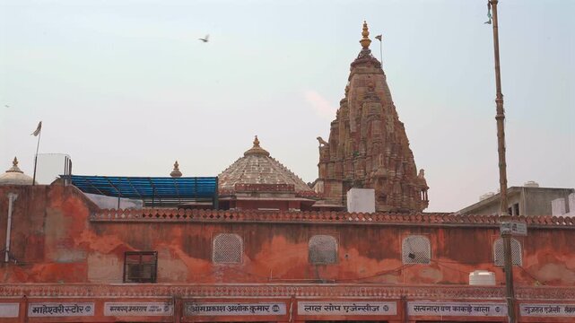 Low angle static shot of a traditional Hindu temple stone spire and dome rising above shop fronts with Hindi signage in Jaipur, Rajasthan, India.