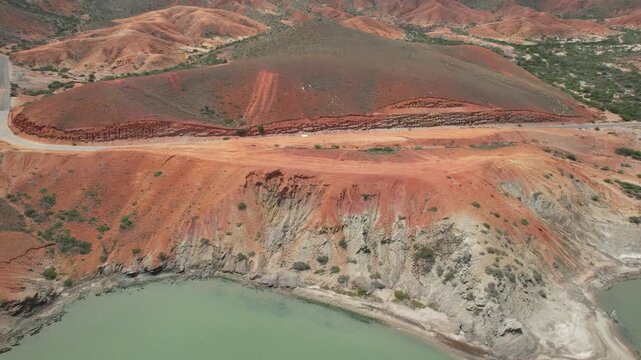Aerial drone shot moves forward over coastal road and red hills by the sea in Araya
