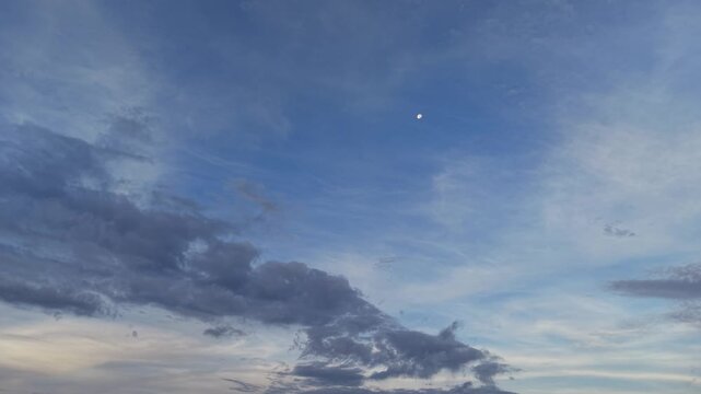 Serene blue sky with wispy clouds and visible moon at twilight, peaceful nature background
