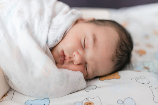 Sweet newborn baby lying comfortable asleep on side wrapped snugly in soft muslin wrap.