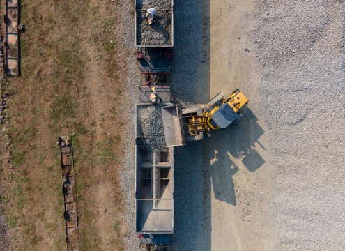 Aerial Construction work of a Yellow Wheel Loader Loading Ballast Rock into a Railway Transport Wagon with Workers Visible on Top in Karangsari, Indonesia. Maintenance Operation Shows Heavy Machinery 