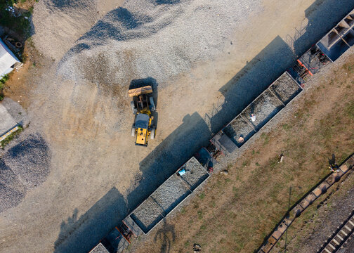 Aerial Construction work of a Yellow Wheel Loader Loading Ballast Rock into a Railway Transport Wagon with Workers Visible on Top in Karangsari, Indonesia. Maintenance Operation Shows Heavy Machinery 