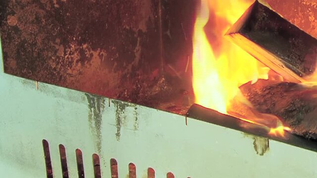 The footage shows burning wood in metal combustion chamber. The shot contains orange yellow fire around dark wooden logs and metal ventilation slots within metal combustion chamber.