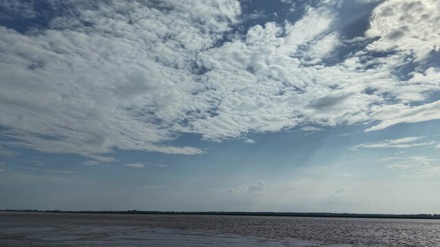 Small boat sailing on wide river under dramatic cloudy sky at sunset, scenic tropical landscape and peaceful water travel