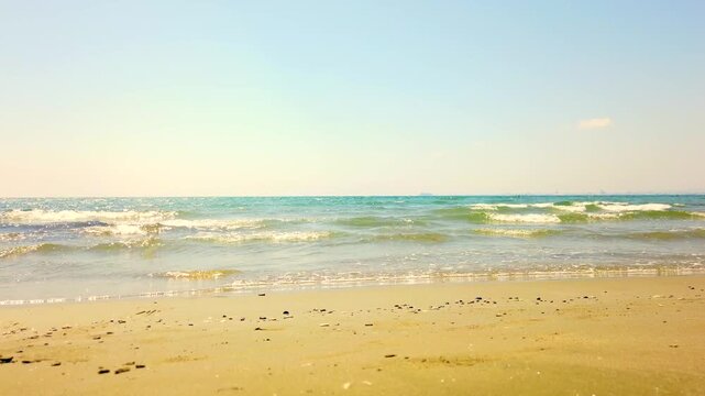Waves wash onto the golden sands of Larnaca beach, Cyprus, with a ship visible far out at sea on the horizon.