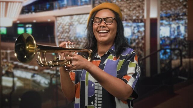 Young african american woman holding trumpet with fingers on valves, smiling, wearing yellow beret, patterned shirt and glasses in building; joyful performance.