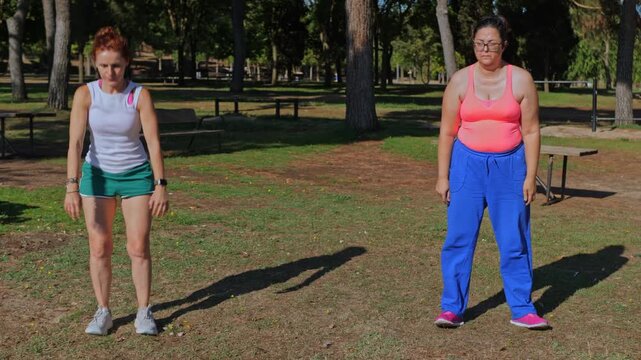Male fitness coach adjusting form and encouraging two women performing bodyweight squats in an outdoor park on a sunny day.