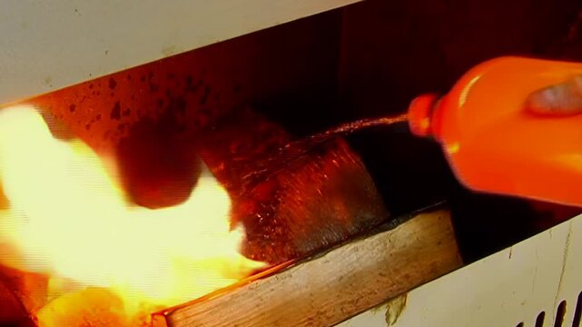 The footage shows wooden logs and flames in vented metal chamber. The shot contains orange yellow fire around dark wooden logs and metal ventilation slots across the visible setting.