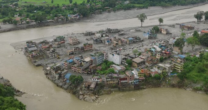 Nuwakot, Nepal, drone shot of extensive flash flood damage across a river peninsula village, with homes and structures surrounded by muddy floodwaters and thick silt after a glacial outburst in Tibet