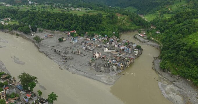 Nuwakot, Nepal, aerial shot of flash flood inundation across a riverside settlement, with submerged homes and heavy mud accumulation surrounded by mountain valleys near Trishuli river