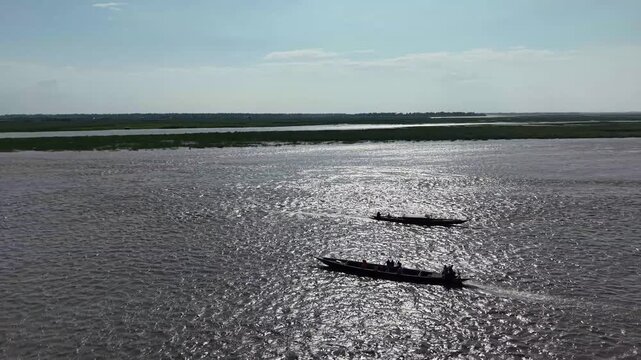 Traditional wooden boats navigating a wide tropical river at sunset, aerial view of rural waterway transportation and scenic nature landscape