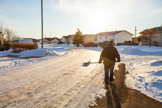 Man carrying a shovel walks down a snowy suburban street