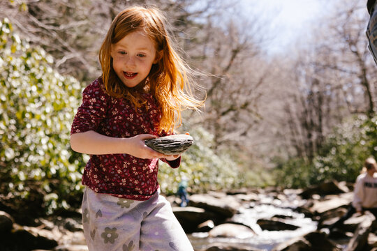 Happy girl with red hair finds a cool rock by a stream
