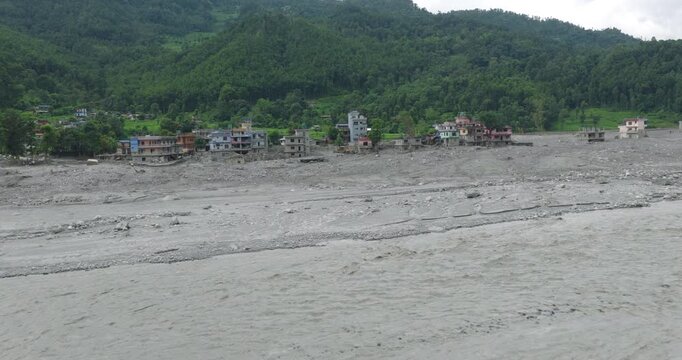Betrawati Nepal, aerial shot of severe post-disaster devastation, with a massive bed of grey mud silt and debris covering the landscape in front of residential structures after a glacial outburst