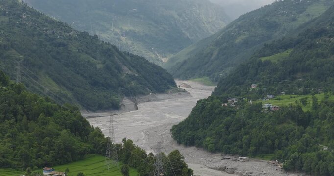 Drone shot of Betrawati, Nepal, of a mountain valley corridor where the swollen Trishuli River flows with heavy mud silt deposits after a glacial outburst disaster.