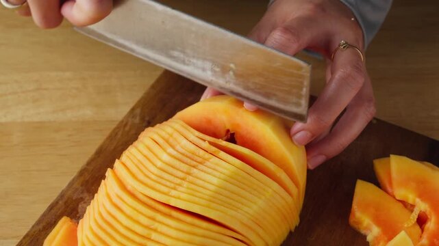 Person thinly slicing fresh unripe papaya on a wooden cutting board