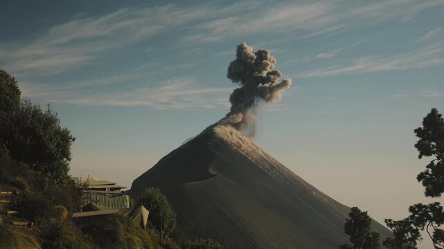 Fuego Volcano erupting in Guatemala, with a huge ash plume rising above the peak. Golden hour light illuminates the volcanic slopes and lush foreground.
