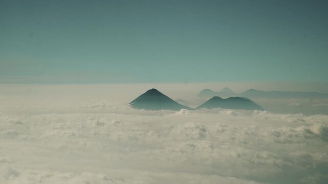 Volcanoes and surrounding peaks towering above rolling low clouds and ethereal mist.