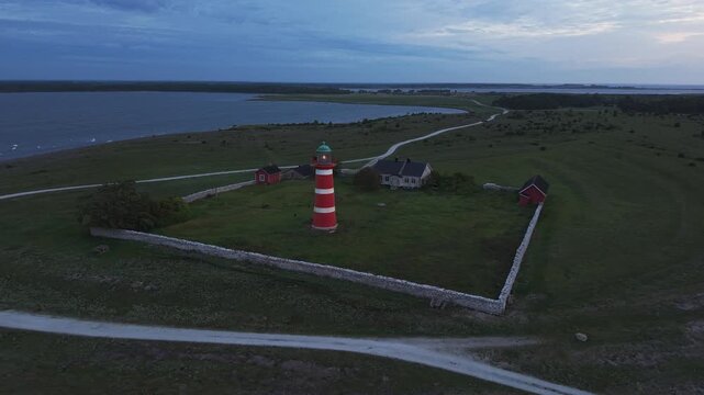 Aerial view of a lighthouse station with keeper's house, stone walls and outbuildings surrounded by open coastal grassland on Gotland during early morning light.