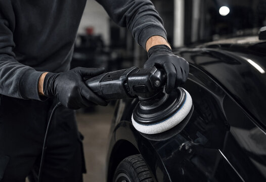 Person polishing car using electric buffer machine in garage setting
