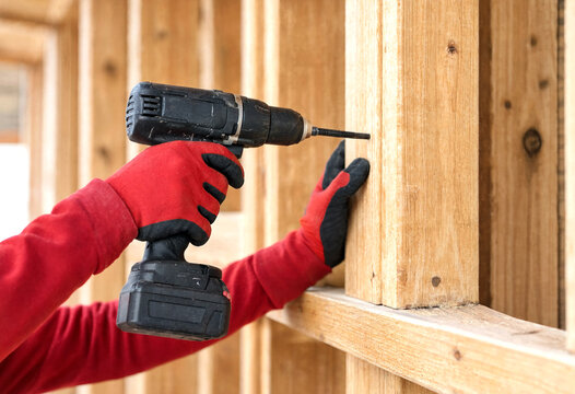 Person using power drill to assemble wooden wall framing indoors