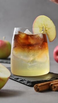 Hand garnishes apple cider cold brew tonic with apple slice and adds glass straw to iced drink.